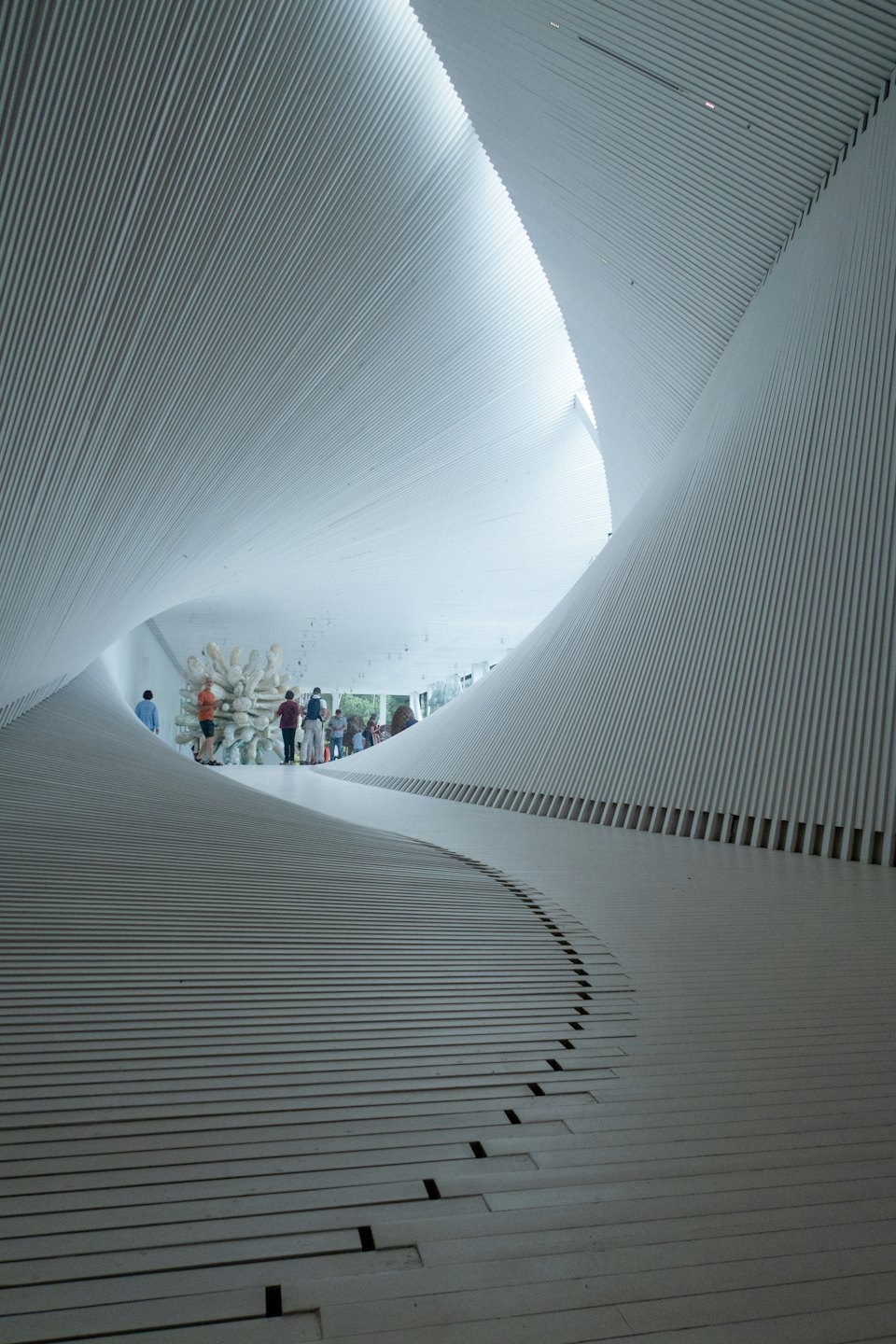 Visitatori passeggiano in una galleria d'arte moderna con pareti bianche curve.