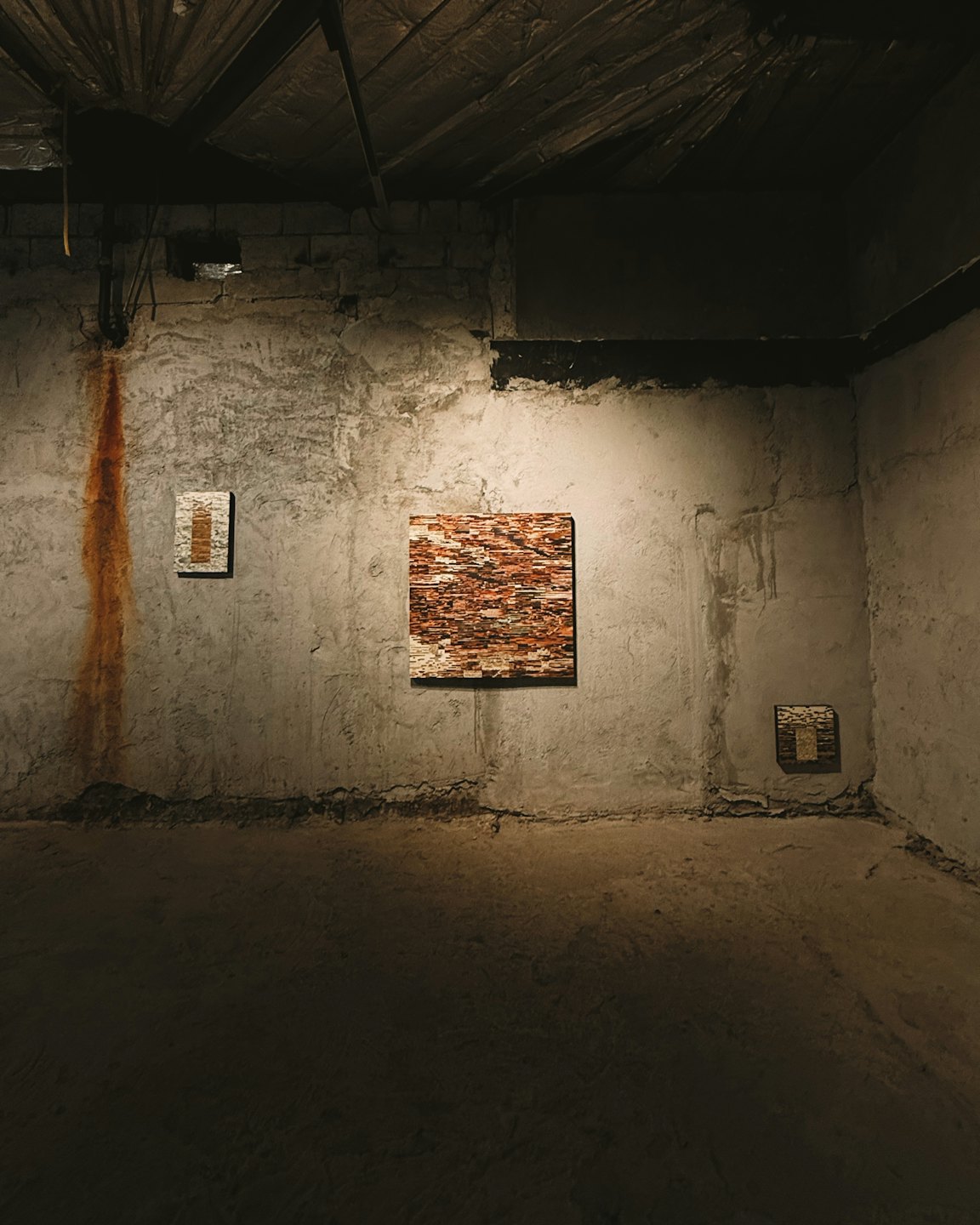 Tre quadri astratti appesi a un muro di cemento grezzo.