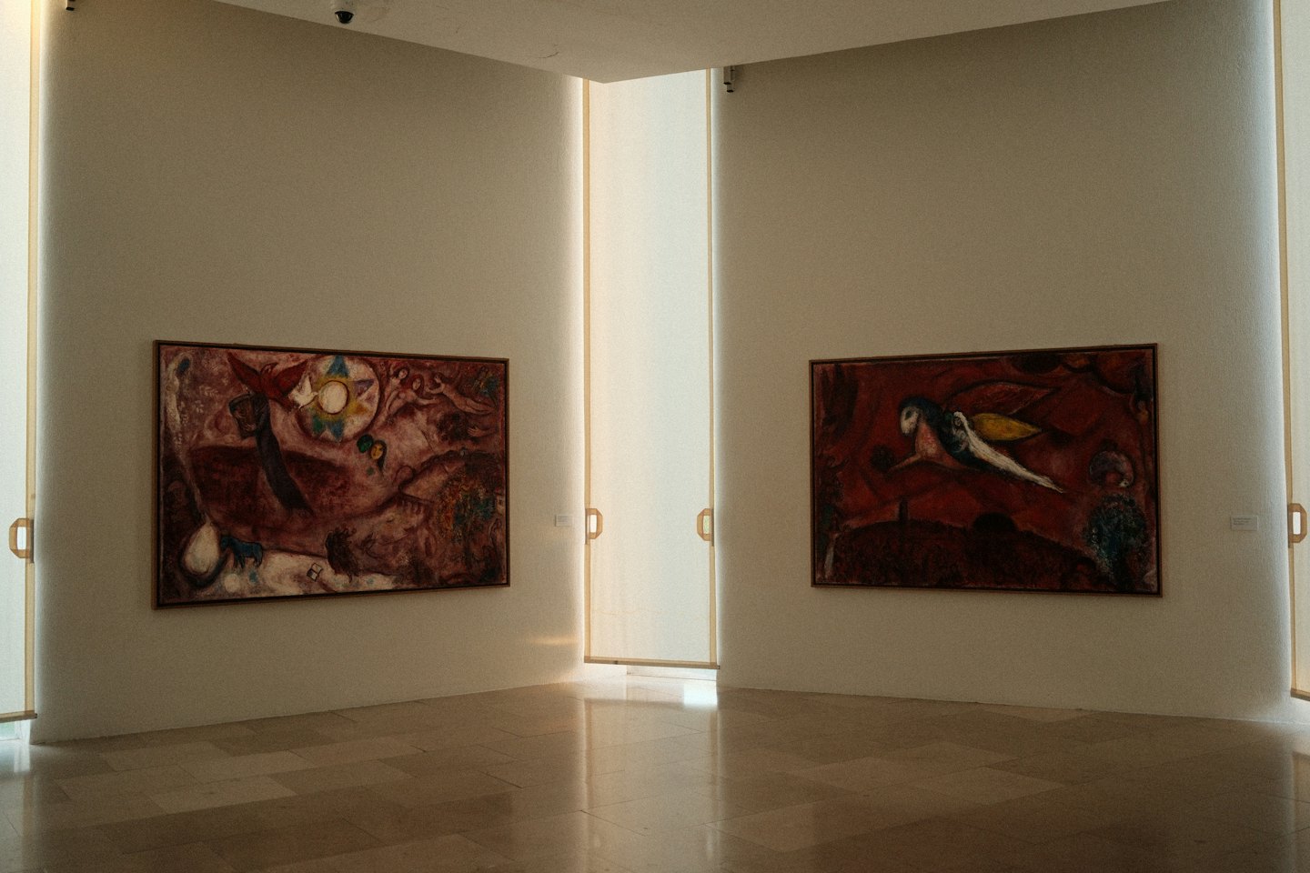 Due quadri astratti sono appesi alle pareti di una galleria sopra pavimenti piastrellati.
