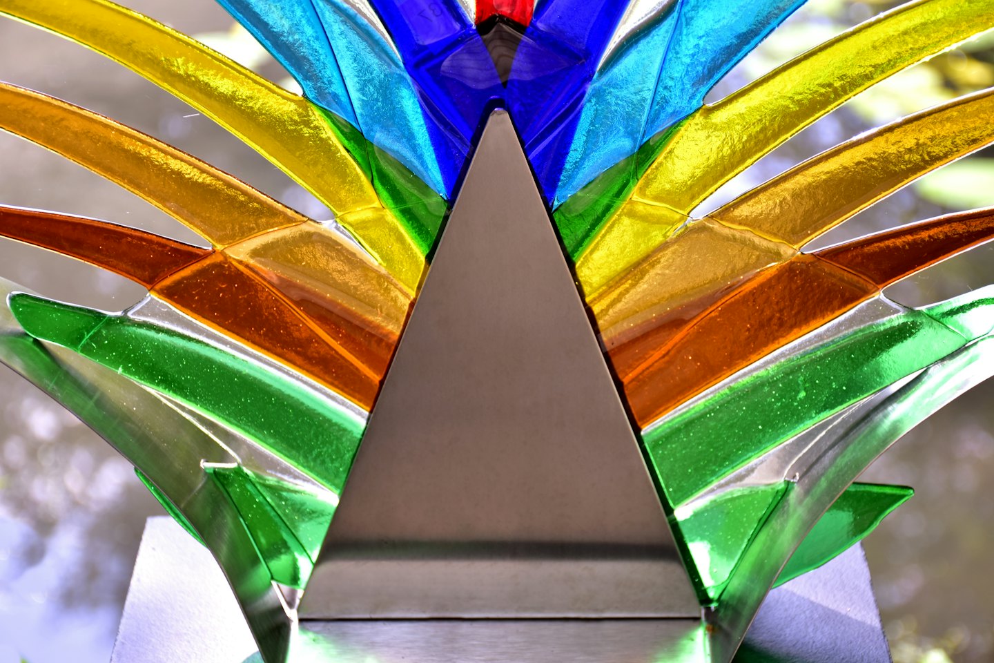Scultura astratta con segmenti traslucidi colorati e triangolo metallico.